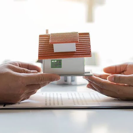 Entrega de una casa: manos sosteniendo una maqueta sobre el contrato